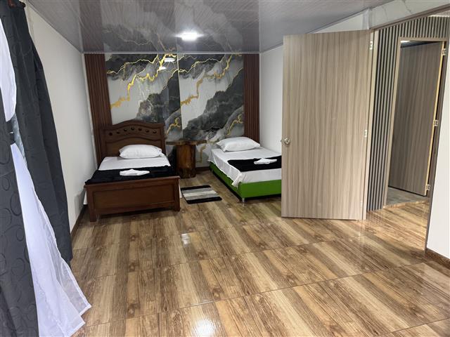 Hotel room with two single beds, white linens and folded towels, dark wood headboard and green frame, marble wall behind, wood floor, open door.